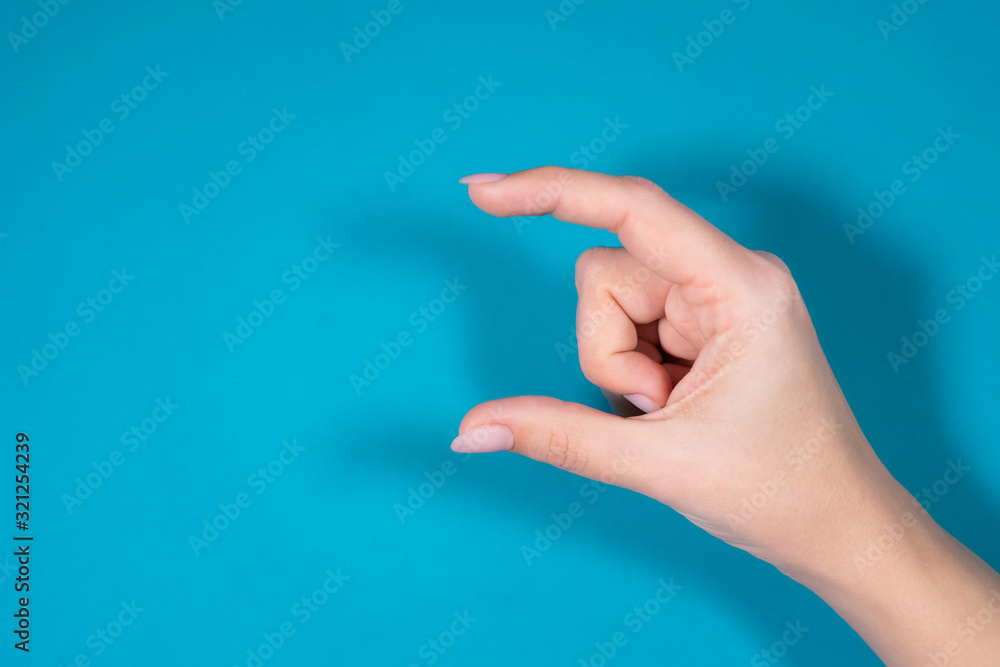 Closeup view horizontal photography of 1 female hand forming gesture as if showing size of virtual invisible object with help of two fingers isolated on bright blue color background. Closeup view horizontal photography of 1 female hand forming gesture as if showing size of virtual invisible object with help of two fingers isolated on bright blue color background.