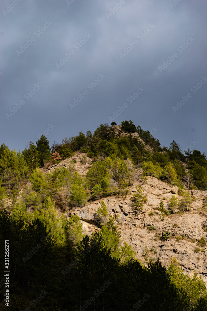 The high-contrast view of the low French Alps under the warm sunlight against the background of the cloudy dark sky