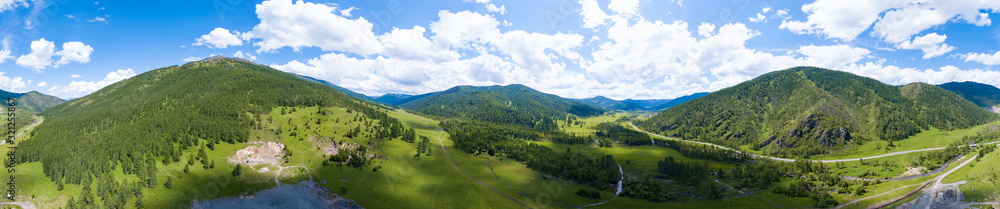 Aerial panoramic banner view of landscape with mountains, green trees, field, road and river under blue sky and clouds in summer
