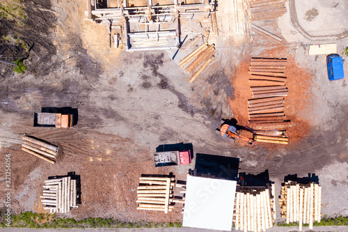 Aerial view of the construction site during the building of a wooden house from thick beams of sawn trees with construction equipment, tractors and trucks. Deforestation and woodworking industry.