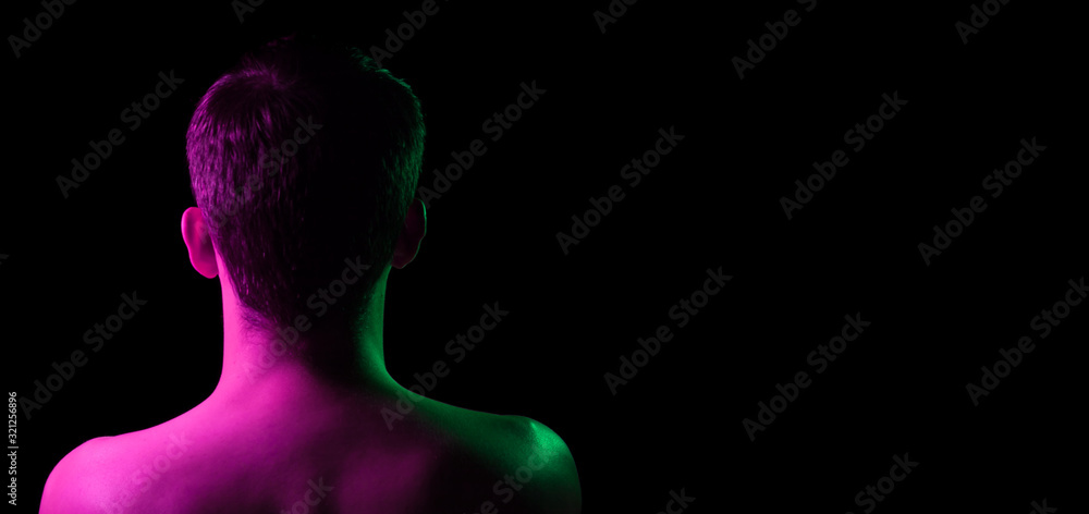 Close-up of the nape, back and shoulders of an short hair head of a man with stubble, naked without clothes, illuminated on one side in pink and on the other green on a black isolated background Close-up of the nape, back and shoulders of an short hair head of a man with stubble, naked without clothes, illuminated on one side in pink and on the other green on a black isolated background