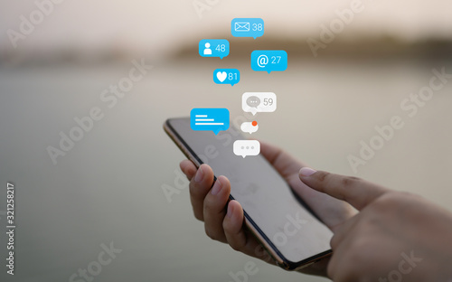 Person using a social media marketing concept on mobile phone with notification icons of like, message, comment and star above smartphone screen.