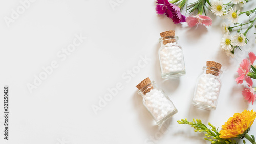 Homeopathic globules​ bottle with wildflowers​ on white backgound. Homeopathy alternative medicine concept. Flat​ layout. Copy space. photo