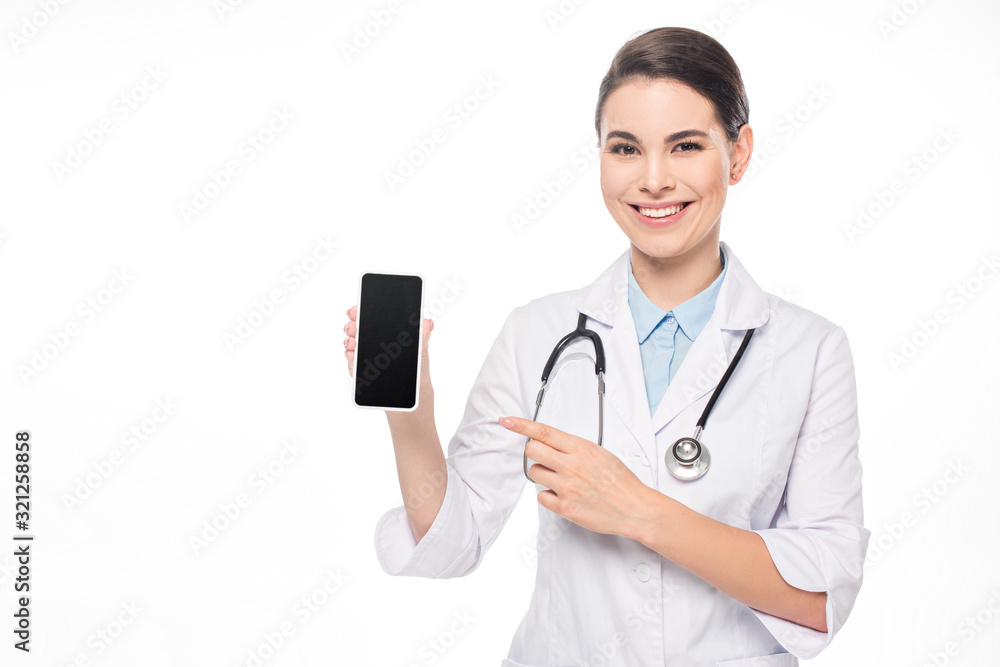 Attractive smiling doctor pointing at smartphone isolated on white Attractive smiling doctor pointing at smartphone isolated on white