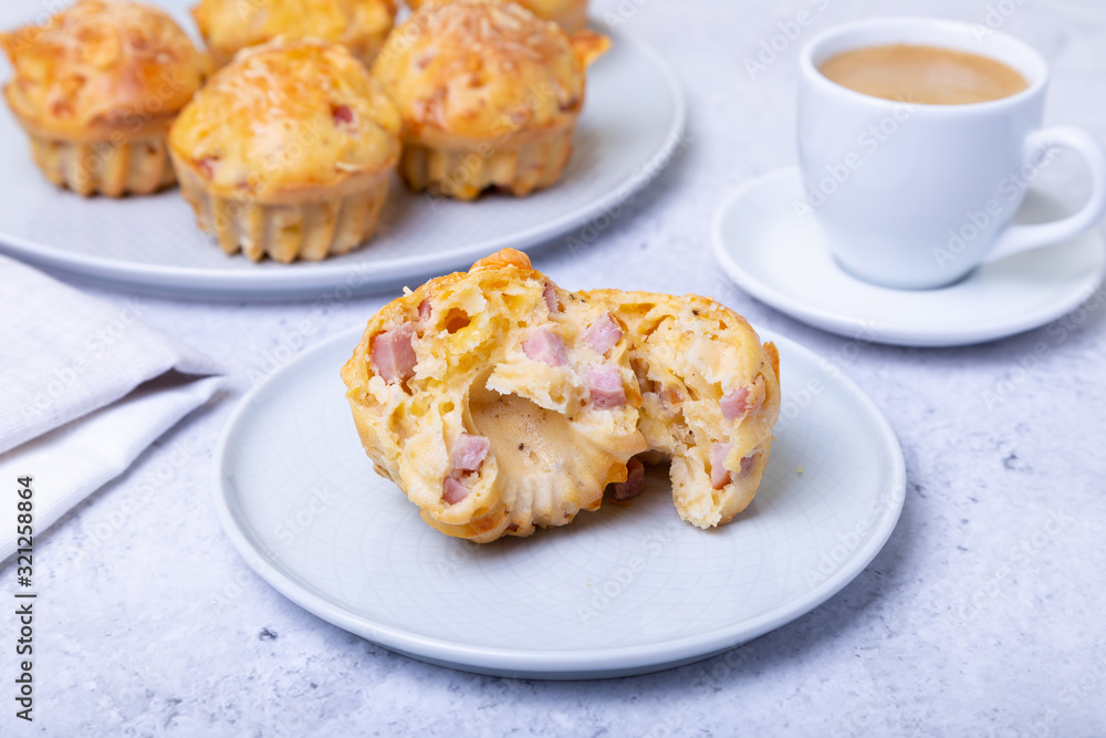 Muffins with ham and cheese. Homemade baking. In the background is a plate with muffins and a cup of coffee. Close-up. Muffins with ham and cheese. Homemade baking. In the background is a plate with muffins and a cup of coffee. Close-up.