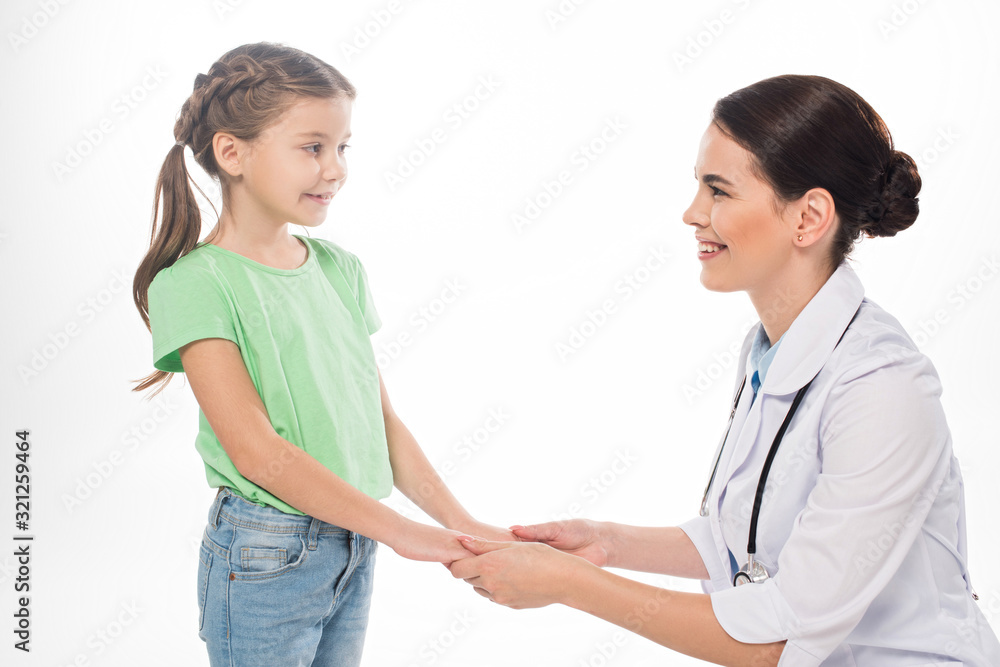 Side view of pediatrician and kid holding hands and smiling at each other isolated on white Side view of pediatrician and kid holding hands and smiling at each other isolated on white