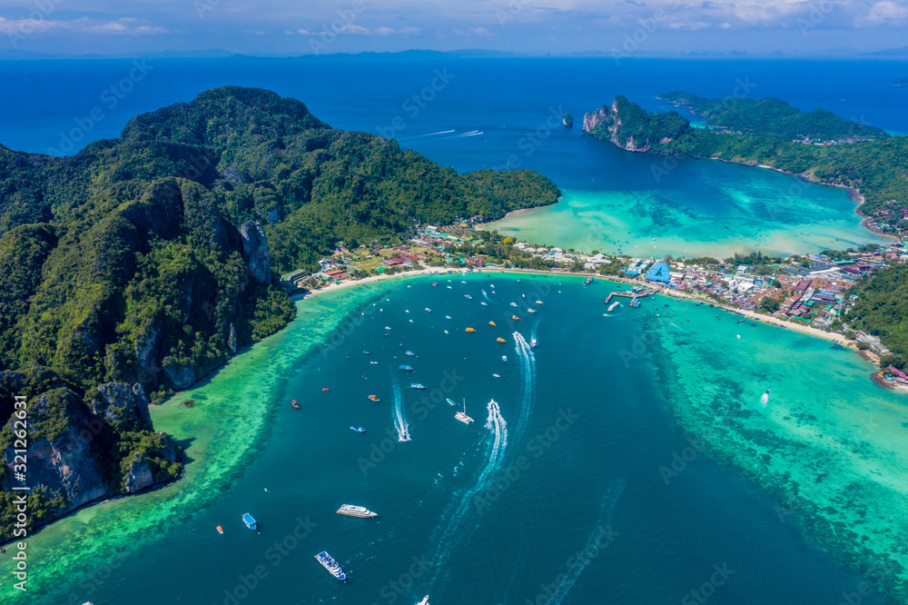 Blue clear water with boats. Green tropical island Phi Phi, palm trees grow. Shooting from a drone from the air. Beautiful seascape. Turquoise color of the water, you can see the bottom and corals.