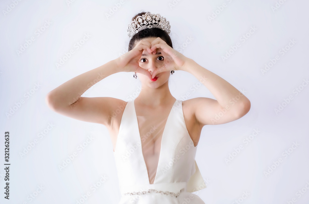 Φωτογραφία Young beautiful woman smiling in love showing heart symbol and shape with hands wearing a white dress and diadem