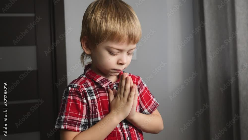 A blond boy prays alone in his room. The child holds his hands together. A blond boy prays alone in his room. The child holds his hands together.