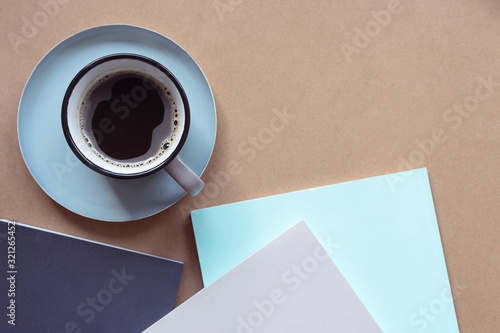 Cup of coffee on a blue saucer. Top view of the workspace. Mock up of three books on the table.