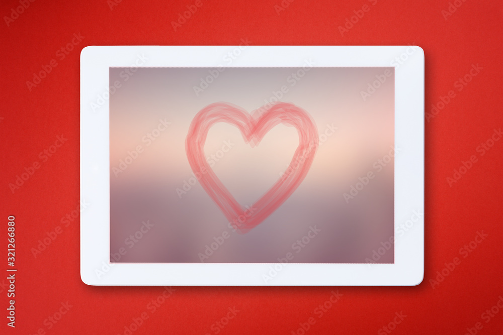 Modern digital tablet with heart shape isolated on red background
