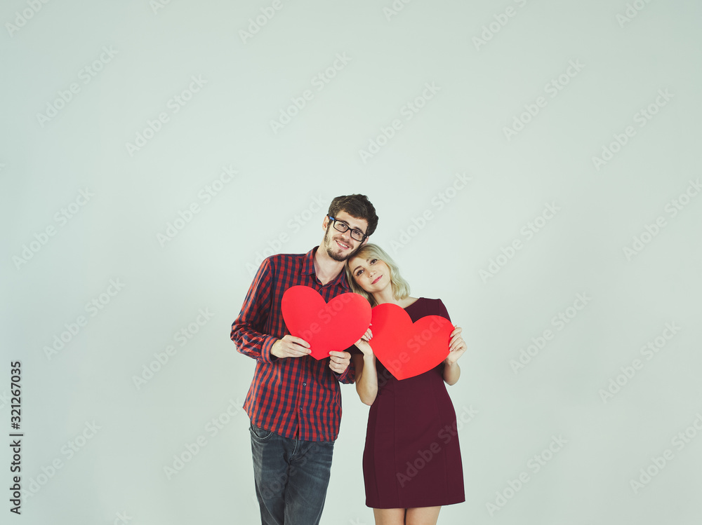 Happy charming couple love in red tone outfits standing, smiling and holding two big red heart paper and a man wears eyeglasses, on white background. Photo toned style vintage. Happy charming couple love in red tone outfits standing, smiling and holding two big red heart paper and a man wears eyeglasses, on white background. Photo toned style vintage.