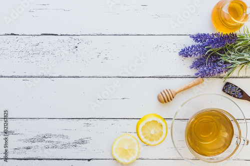 A cup of lavender tea with a jar of honey, honey dipper,  lemon and a bunch of  lavender on white wooden background (Flat lay and copy space)