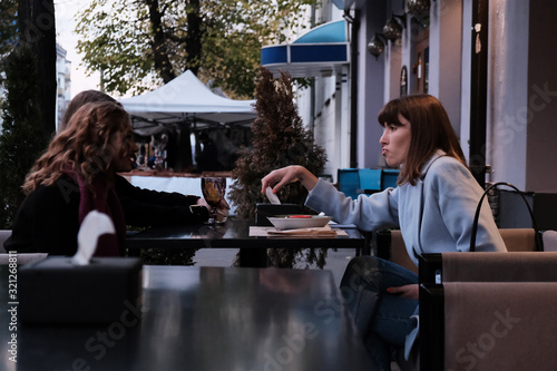 Two pretty girl friends talk and drink tea in cafe  outdoors