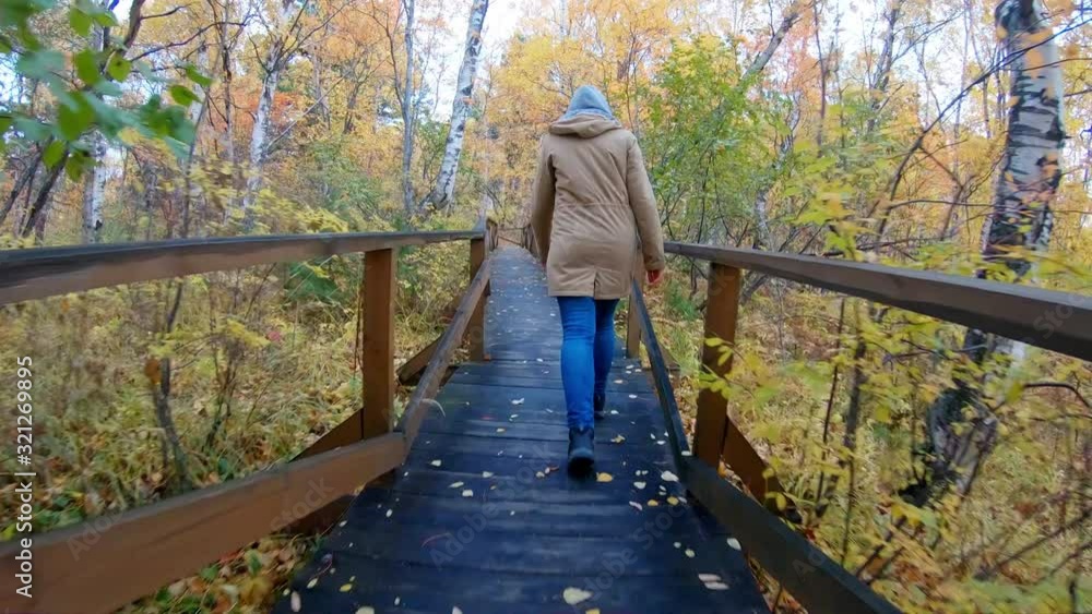 Woman in a hood ascends along an eco trail in the autumn forest. Follow shot, slow motion Woman in a hood ascends along an eco trail in the autumn forest. Follow shot, slow motion