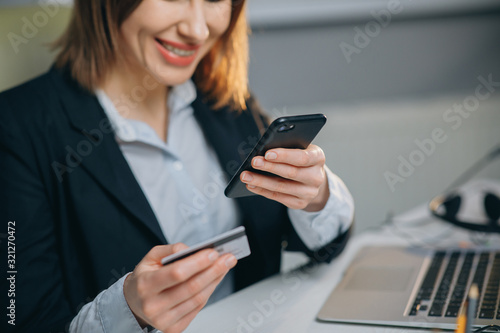 Happy and Smiling Woman Making a Card Payment through Mobile Phone to Pay Bills. An Attractive Girl Putting Debit or Credit Card Details on a Smartphone or Cellphone to Make Online Transaction © uflypro
