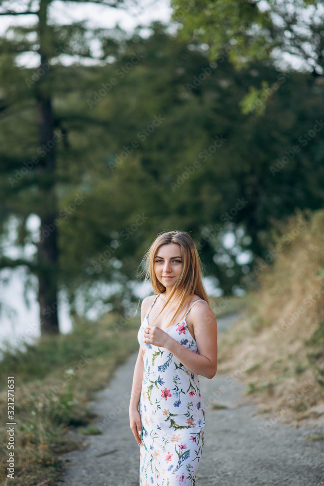 Portrait of young attractive chestnut beautiful woman on green forest background in fresh summer dress