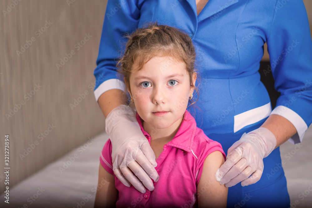 A child is vaccinated. A gloved nurse applies medical cotton to the child’s shoulder. The little girl’s not happy face is after vaccination. Children's medical concept A child is vaccinated. A gloved nurse applies medical cotton to the child’s shoulder. The little girl’s not happy face is after vaccination. Children's medical concept