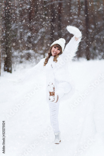 A beautiful pretty young girl with curly hair and a snow-white smile in a white warm coat is walking and fooling around in the winter forest against the background of snow and trees, enjoy