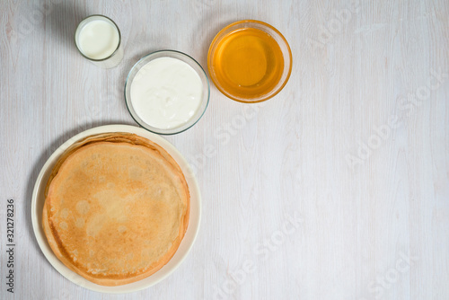 Maslenitsa is a holiday at the end of February . pancakes with honey, sour cream and milk on a light wooden background. honey trickles down a stack of pancakes. close up. blini. space for text.