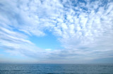 Beautiful sky landscape with white flying clouds extending over the skyline line of the sea surface