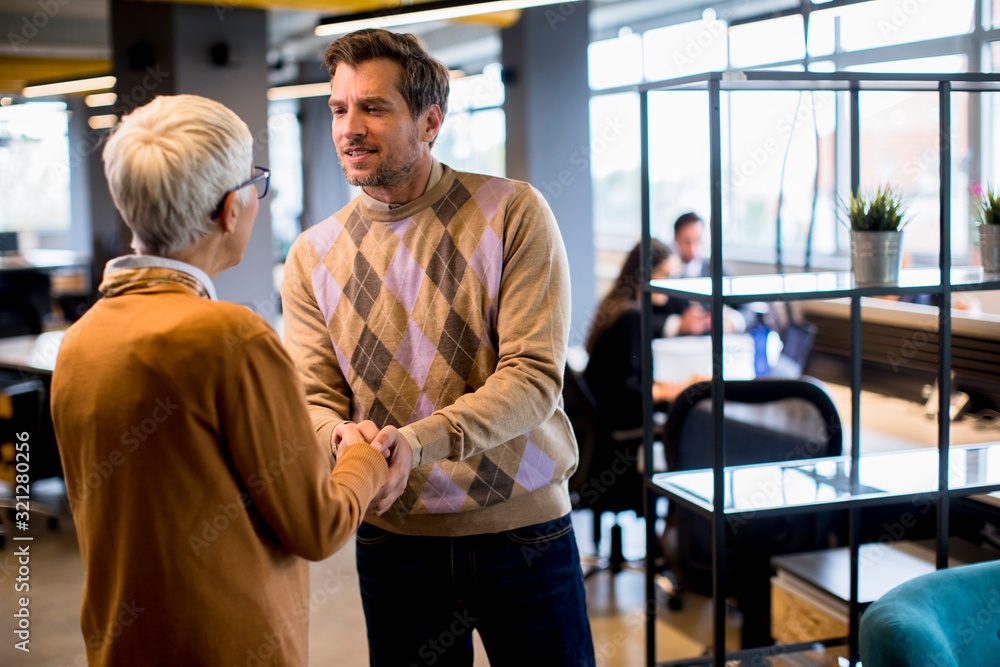 Young business man and senior business woman shaking hands in the office Young business man and senior business woman shaking hands in the office