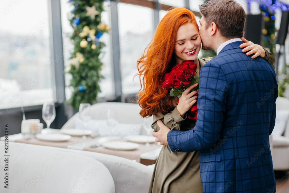 kind and gallant caucasian man in tuxedo invited on a dtae and gave red flowers, roses to his lady in dress. smiling pleasant redhaired woman thanks him. in restaurant kind and gallant caucasian man in tuxedo invited on a dtae and gave red flowers, roses to his lady in dress. smiling pleasant redhaired woman thanks him. in restaurant