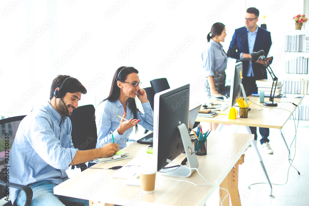 Attractive business people in headsets are smiling while working with computer in modern office Attractive business people in headsets are smiling while working with computer in modern office