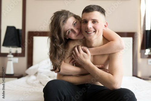 Smiling young woman embracing shirtless boyfriend in bedroom © Ivan
