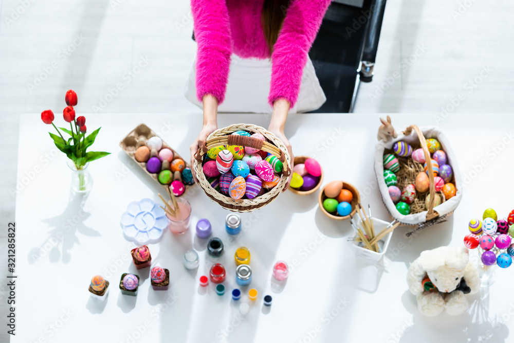 Easter holiday concept,Close up of Happy Asian Young woman hand holding a basket with colorful Easter eggs on white wooden table background in top view