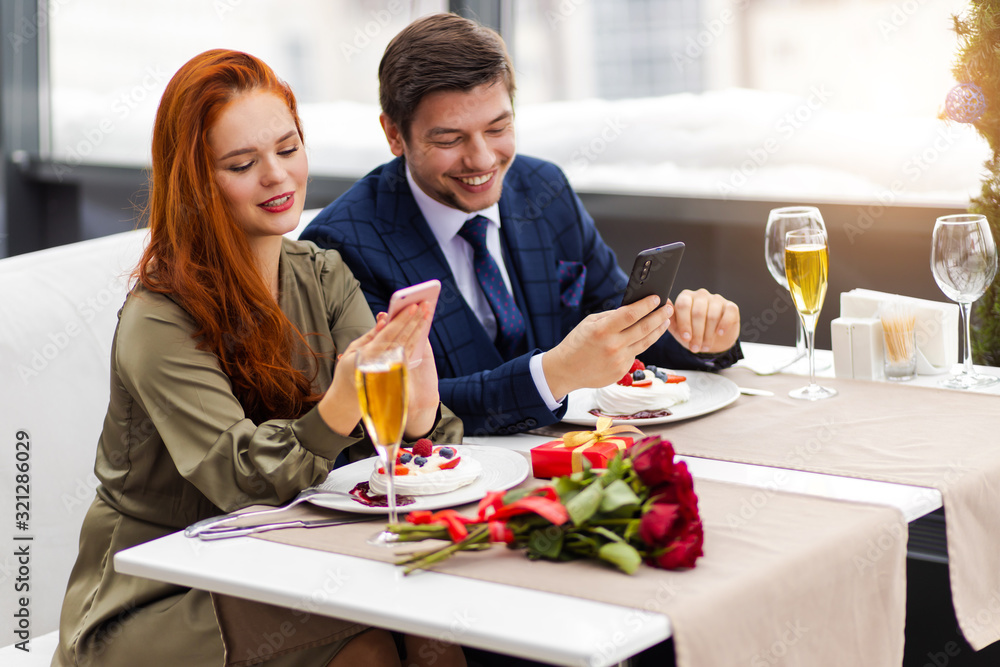 couple celebrate birthday of redhaired woman in restaurant. beautiful lady in dress experiencing vivid emotions with her boyfriend in tux, handsome guy is real gentleman. love, romantic, celebration