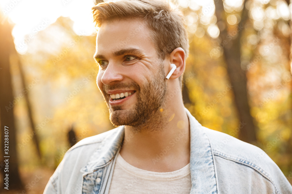 Image of handsome young caucasian man using earbuds while walking in park Image of handsome young caucasian man using earbuds while walking in park