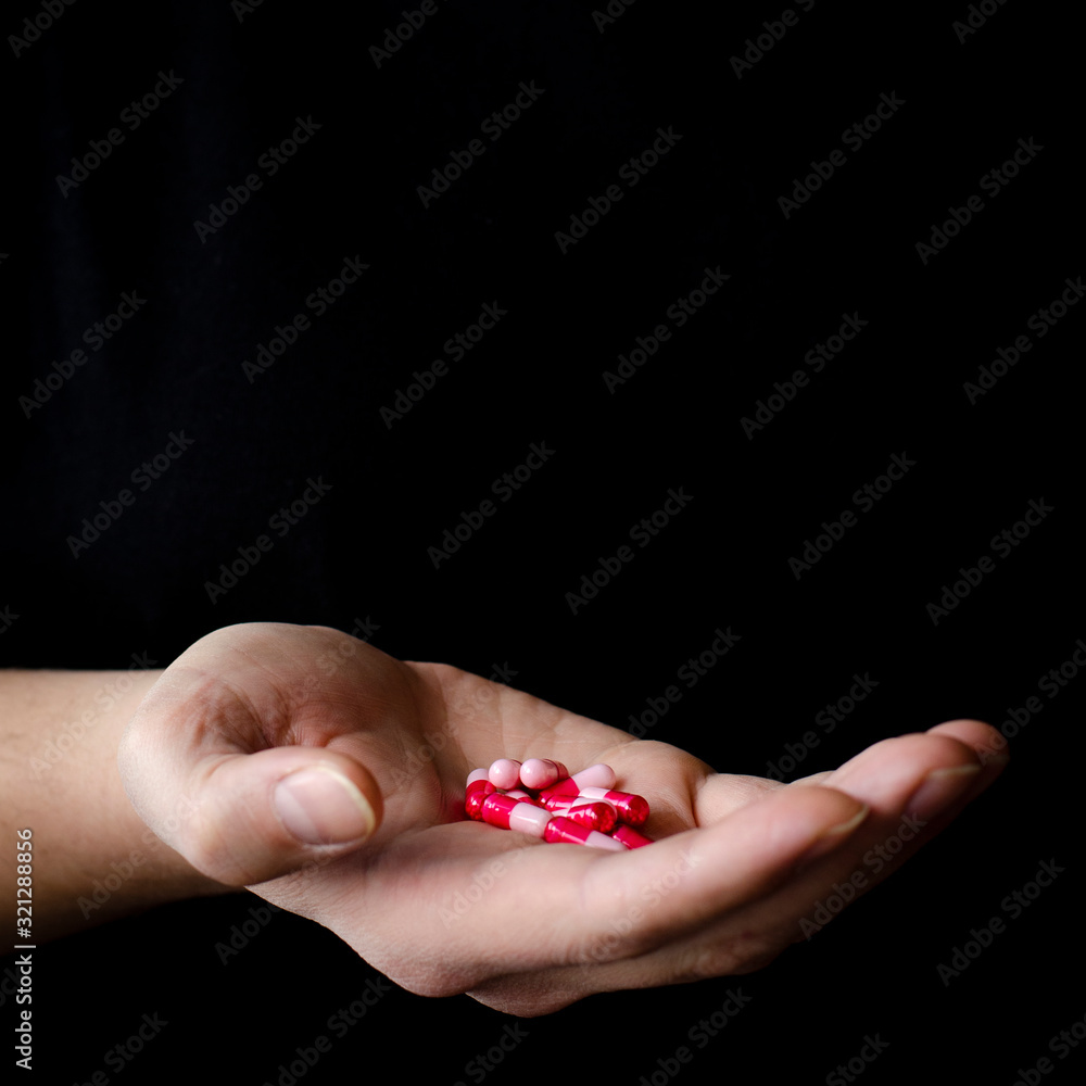 A man's hand in a black T-shirt holds multicolored antiviral tablets.