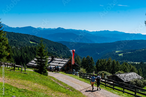 Zwei Wanderer gehen zu einer Almhütte mit Tiroler Fahne und Weitblick in die Bergwelt der Dolomiten photo