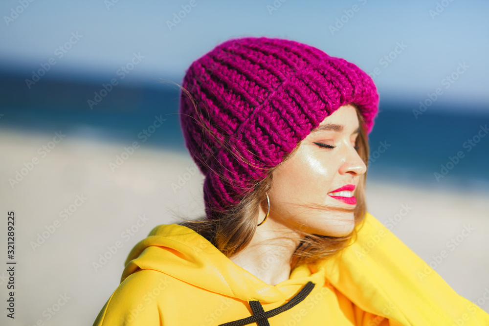 Young beautiful woman in yellow sweatshirt and bright purple knit hat on the beach Young beautiful woman in yellow sweatshirt and bright purple knit hat on the beach