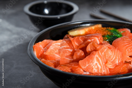 Fresh salmon on rice topped with roe in a black bowl, sprinkled with green seaweed with black sauce, popular in Asia on a marble table background.