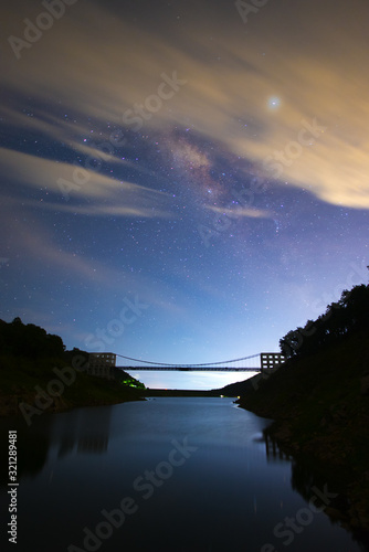 Photograph of beautiful milky way rising over the bridge at the damp in Chiang Mai city, Thailand.