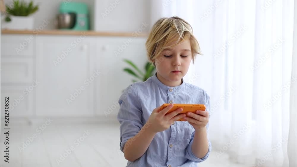 cute blonde boy, cheerful kid playing games on the phone, surfing the internet on gadget cute blonde boy, cheerful kid playing games on the phone, surfing the internet on gadget