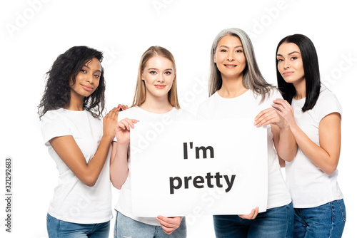 cheerful multicultural women near placard with i`m pretty lettering isolated on white