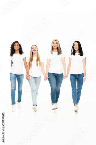 happy multicultural women in denim jeans walking and holding hands isolated on white