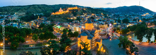 The evening panorama of the old town in the old district of Avlabari, Virgin Mary Metekhi church and Rike Park, the Kura river reflects the evening city lights in Tbilisi, Georgia.