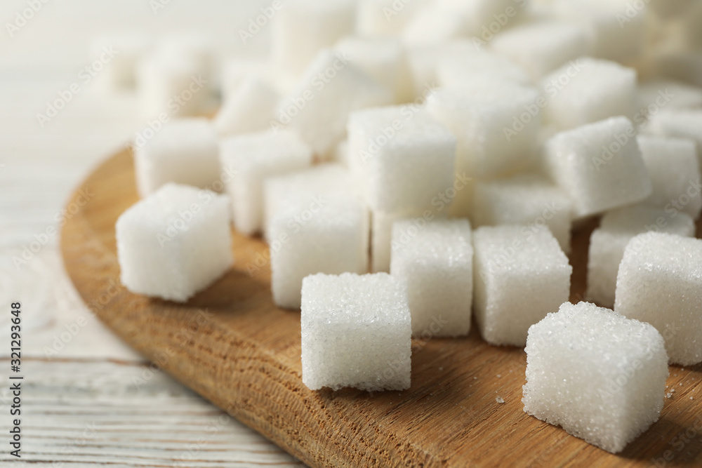 Board with sugar cubes on wooden background, close up