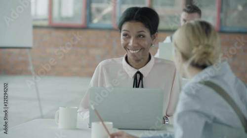 The manager stands near the desktop and communicates with a female employee of the African-American who works with a laptop. Girl smiles. Coworking. Office life. Business