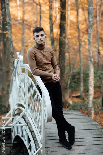 Teen guy walks through the woods in autumn. Pensive and funny teenager. Cute spectacled smiling happy teen boy, looking at camera. Kids outdoor portrait. The guy rests on the railing of the bridge