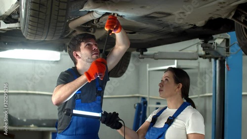 Mechanic in gloves repairs a car, woman holds a flashlight
