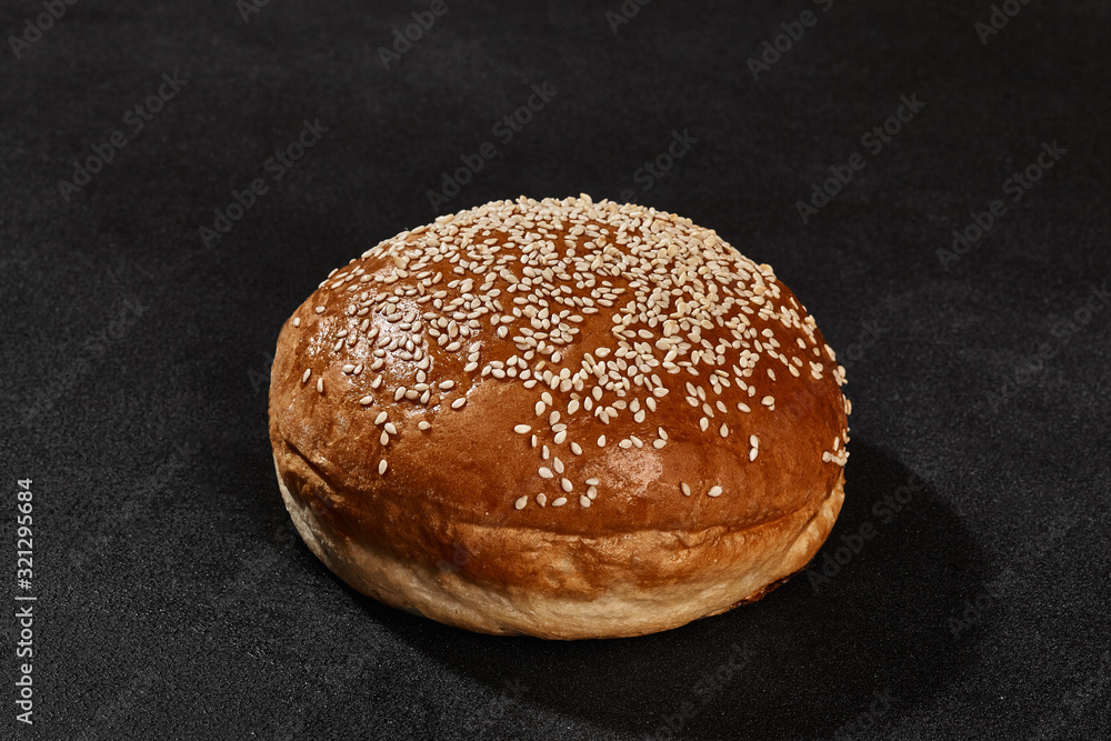 Fresh, tasty baked bun sprinkled with sesame seeds against black background with copy space. Rural cuisine or bakery. Close-up
