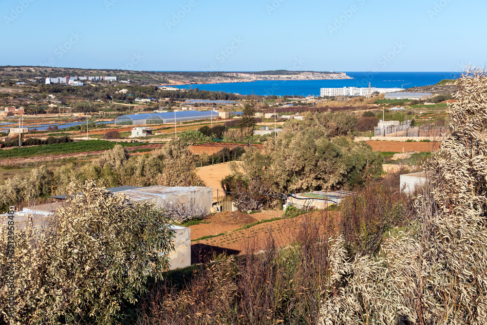 Rural countryside of Malta with dry crop fields, plowed land and blue water of the mediterranean sea bay