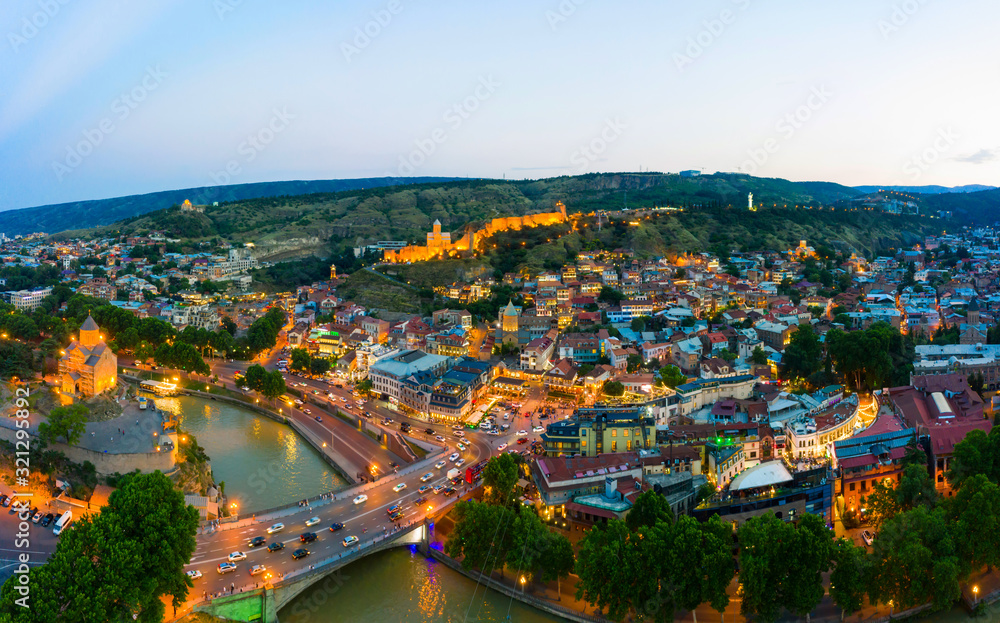 Fototapeta The evening panorama of the old town in the old district of Avlabari, Virgin Mary Metekhi church and Rike Park, the Kura river reflects the evening city lights in Tbilisi, Georgia.