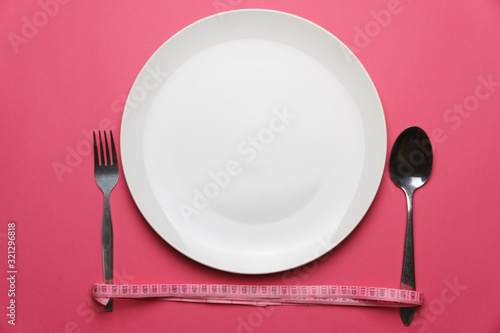 dieting and health care concept. top view of a fork and spoon wrapped with measure tape beside the white plate on pink dine table. flat lay. free copy space for your text