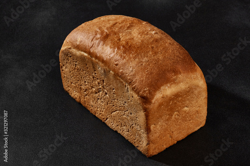 Whole loaf of fresh, palatable baked white bread against black background with copy space. Close-up photo